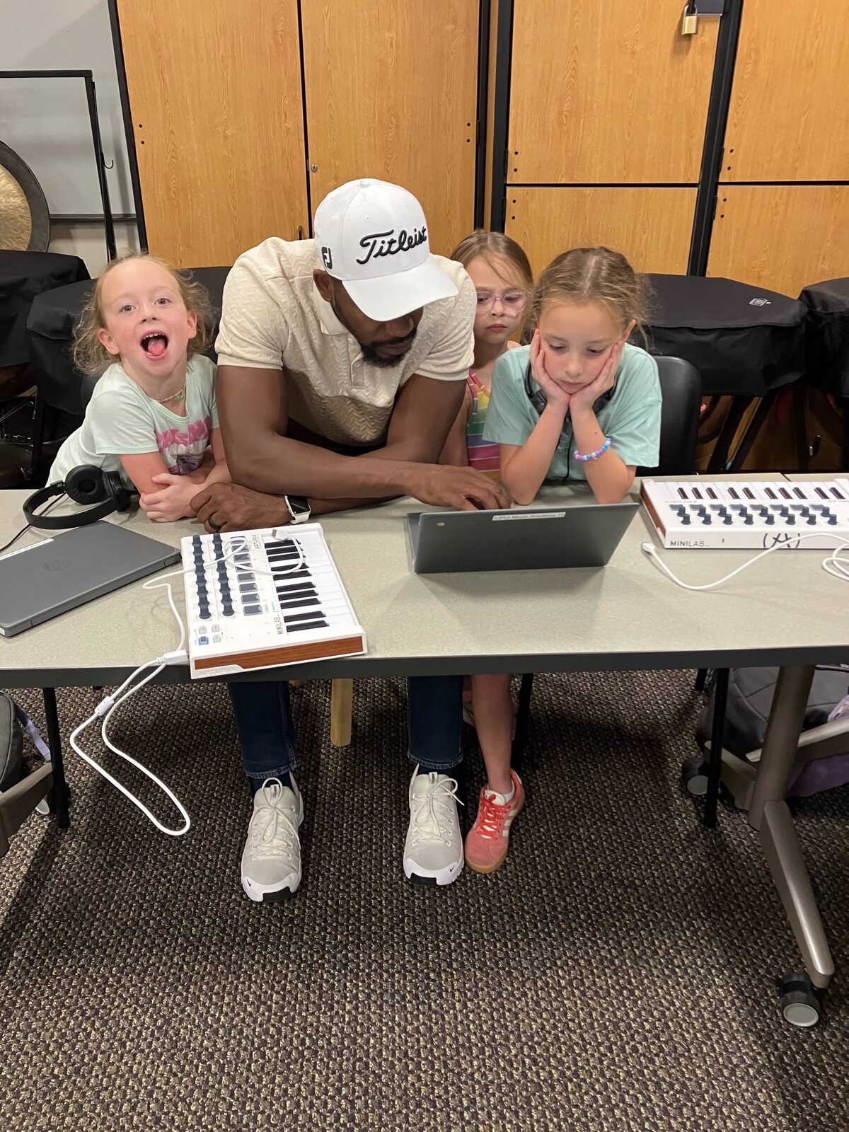 An instructor leaning over students working at a row of MIDI keyboards