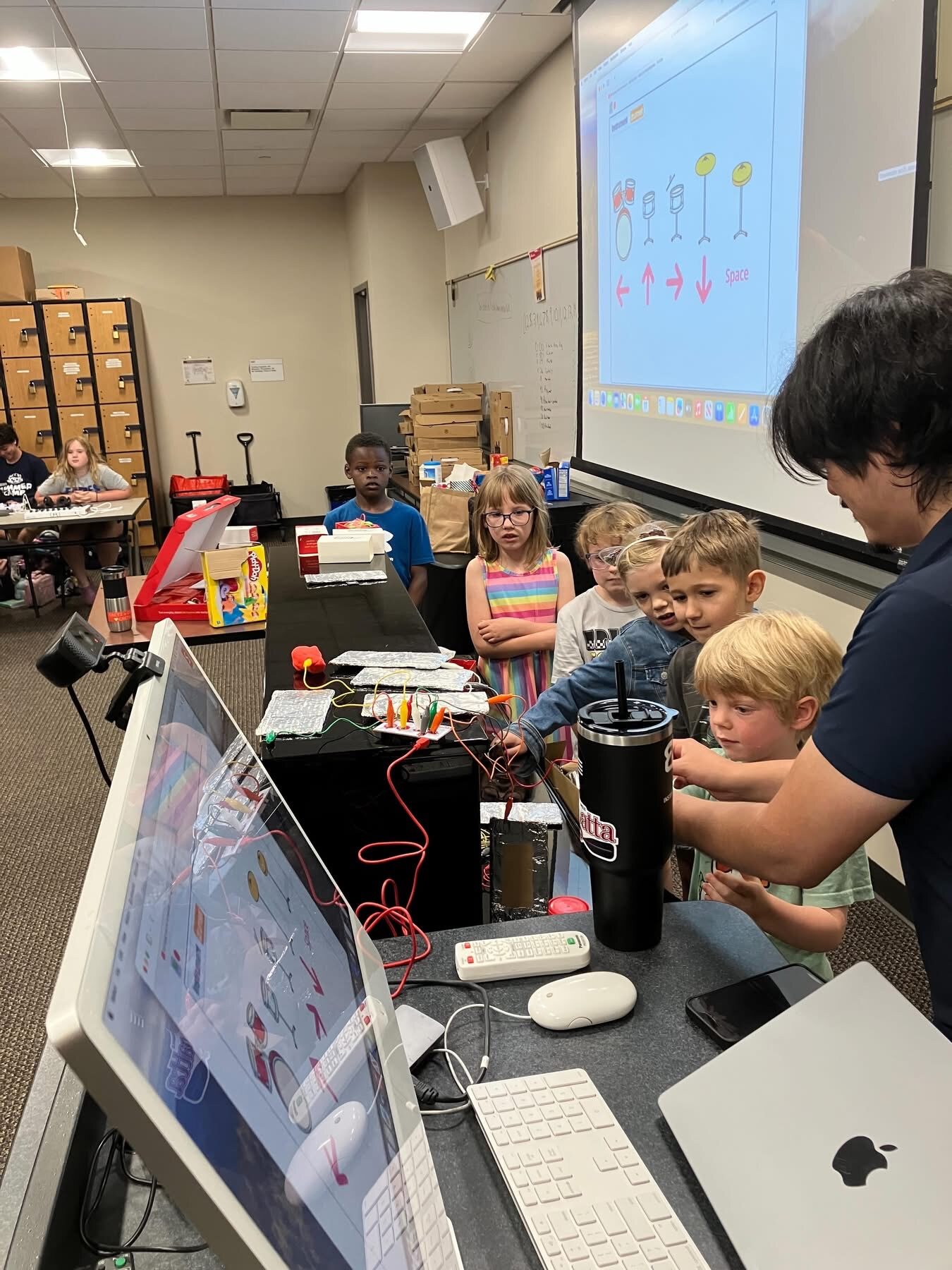 A group of students gathered around a screen learning a MakeyMakey project