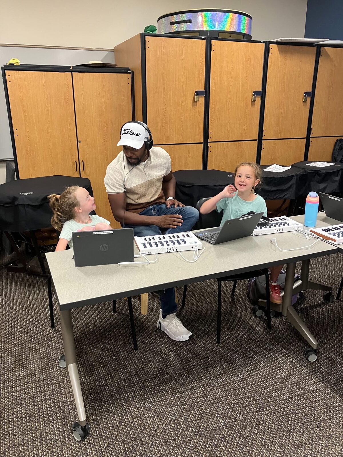 An instructor working with three young students at a Chromebook, one laughing