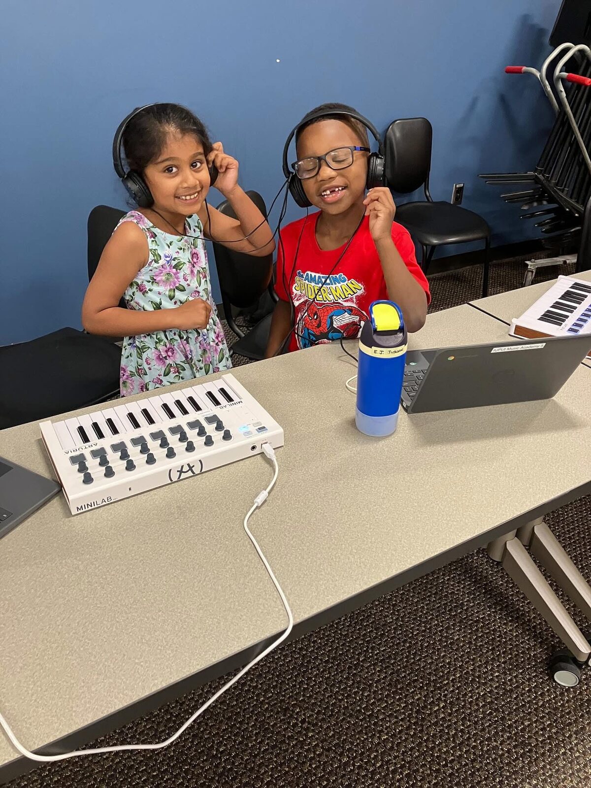 Two young students smiling with headphones and a MIDI keyboard